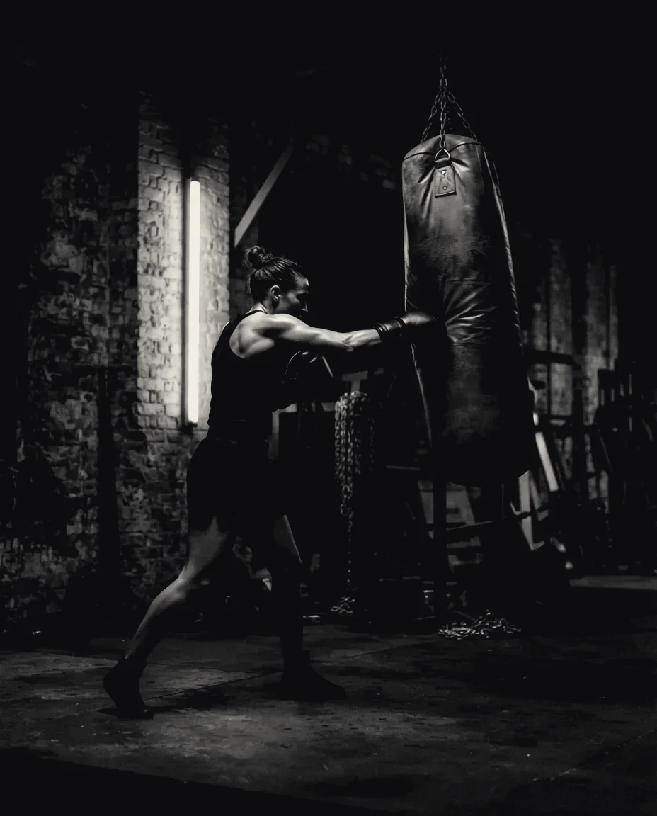 A boxer throwing a gloved cross into a heavy bag in a dark brick-walled gym