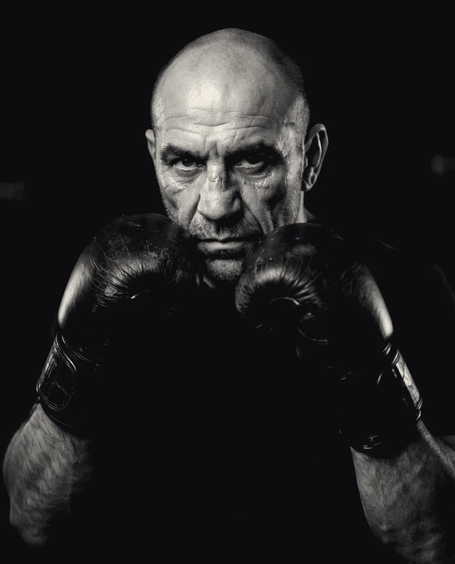 Portrait of a boxing coach holding a high guard in worn leather gloves